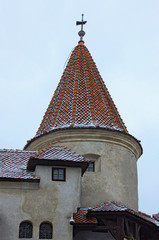 Close up view of ancient tower with red tile roof in the snow, against cloudy sky. Famous Bran Castle, also called Dracula's Castle. Famous touristic place and travel destination in Romania