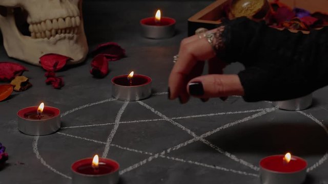 Female hand extinguishing the flame of a candles above the pentagram circle.