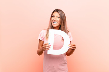 young pretty woman excited, happy, joyful, holding the letter D of the alphabet to form a word or a...