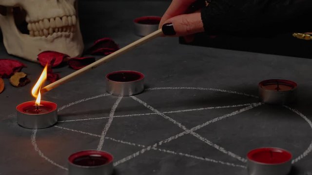 Female hand lights red candles .Magical ritual with occult symbols. 