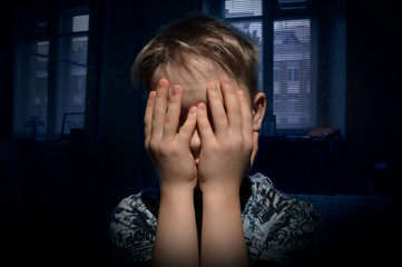 child in a dark room with a window with closed eyes