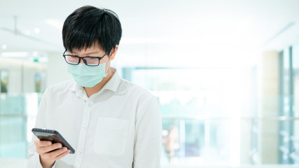 Fototapeta na wymiar Male Asian patient wearing surgical mask using smartphone in hospital or medical center. Medical exam or body check up. Wuhan coronavirus (COVID-19) outbreak prevention. Health care concept