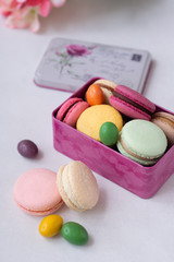Colorful macarons and candy into pink gift box on the white background with flowers. Macaroons close up.