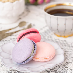 Pink and purple macarons on a white table with flowers, tea or coffee. Macaroons close up. Side view.