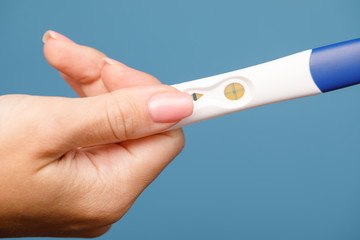 Woman holding holding positive pregnancy test against blue background
