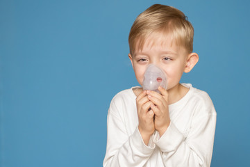 A strabismus boy doing inhalation with a nebulizer on a blue background.