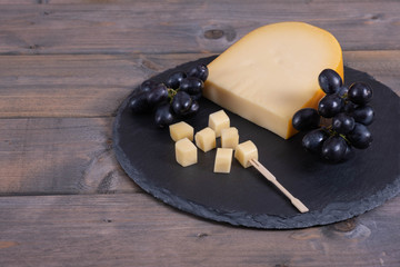 a piece of cheese and grapes lie on a stone
