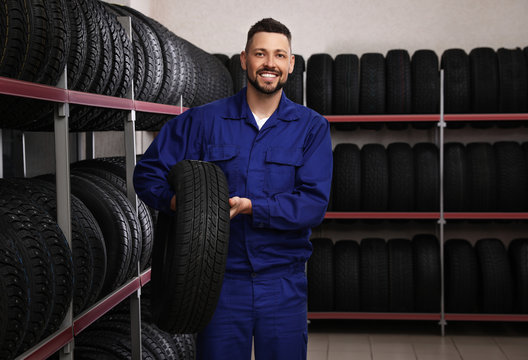 Male mechanic with car tire in auto store