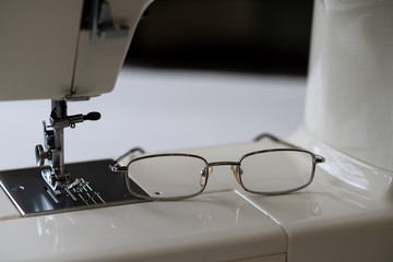Glasses for vision lie on the platform of the sewing machine. Selective focus.