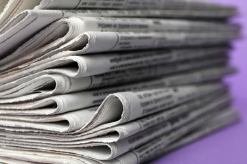 Stack of newspapers on light violet background, closeup. Journalist's work