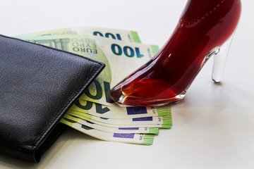 An elegant woman's Shoe stepped on the money protruding from a man's wallet. Copy space.