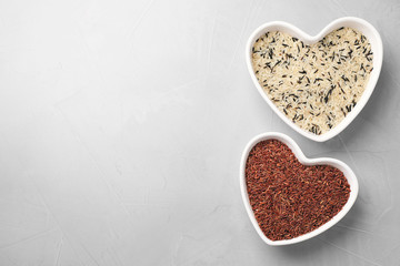 Brown and polished rice in heart shaped bowls on light grey table, flat lay. Space for text
