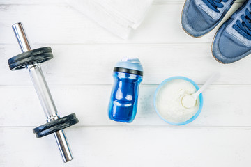 Fitness equipment. Sneakers, water, dumbbells and proteins on white wooden background.