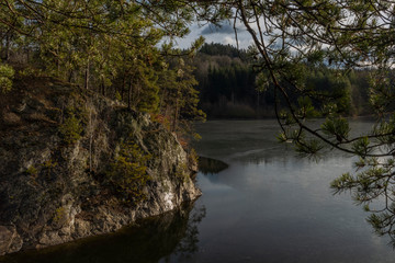 Fototapeta na wymiar Island on Rimov damn with rocks and pine trees in winter sunny day