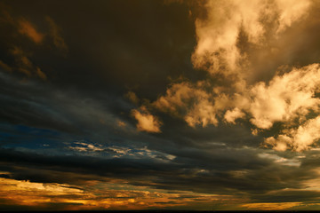 beautiful dramatic sky with dark and bright clouds at sunset, summer landscape, golden sunlight