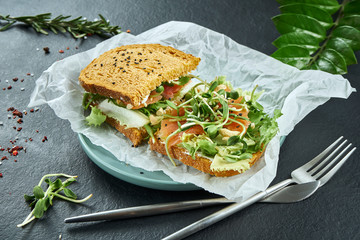 Trendy street snack. Tasty sandwich toast with salmon and microgreen on craft paper on a black background. Close up. Flay lay food with copy space. Seafood