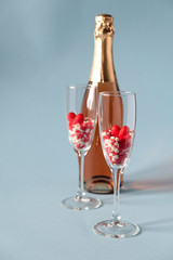 Two champagne glasses with red heart shaped sugar candy and champagne bottle. On blue background. Valentines Day, anniversary or wedding celebration concept.  Copy space.