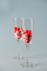 Two champagne glasses with red heart shaped sugar candy. Over blue background. Valentines Day, anniversary or wedding celebration concept.  Copy space.
