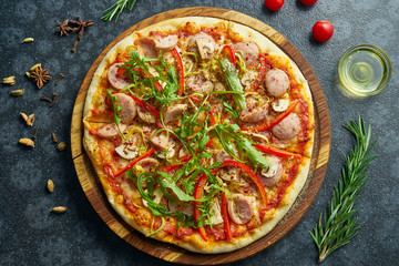 Homemade baked pizza with four kinds of meat, melted cheese, red sauce, tomatoes and ruccola on a black background in a composition with ingredients. Top view flat lay