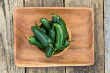 a pile of large spicy green organic Jalapeños on a wood tray