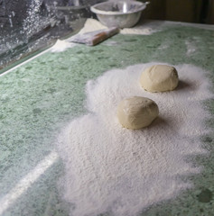 A lump of pizza dough lies in flour on the kitchen table, a blank for baking