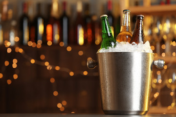 Beer in metal bucket with ice on table against blurred lights. Space for text