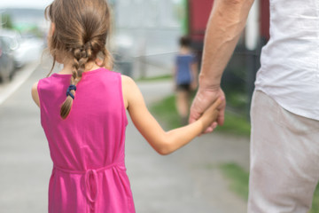 A man in bright clothes leads a little girl by the hand along the street