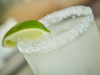 Glass rim garnished with salt and slice of lime , margarita drink light green , shallow depth of field