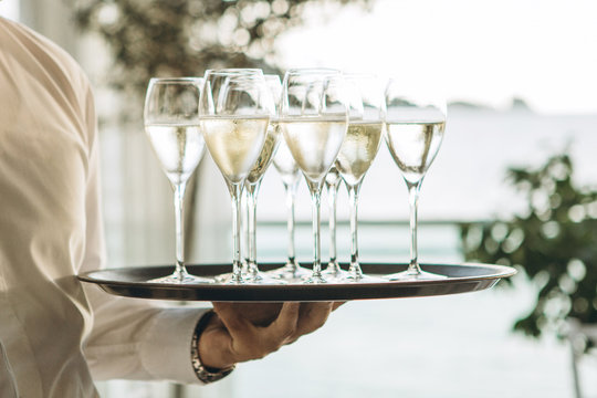 The waiter is holding a tray with glasses of champagne or white sparkling wine. Service in the restaurant.