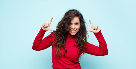 Obraz premium young pretty woman framing or outlining own smile with both hands, looking positive and happy, wellness concept against blue wall