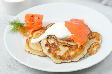 Fritters with salted salmon and sour cream.  A plate with pancakes occupies the entire space of the frame.  Macro shot.