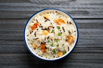 Delicious rice pilaf with chicken on black wooden table, top view