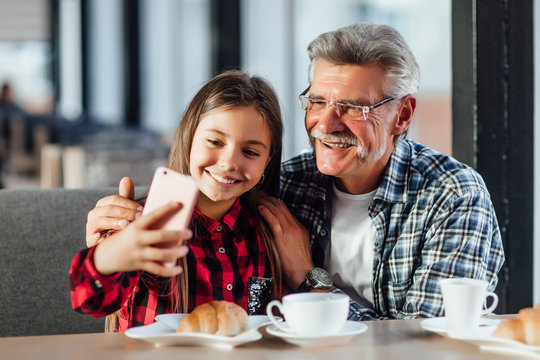 Cute stylish granddaughter wearing red shirt make a selfie with grandfather and croissant, having breakfast together. - Powered by Adobe