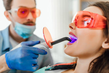 Medicine, dentistry and healthcare concept, dentist male using dental curing UV lamp on teeth of...