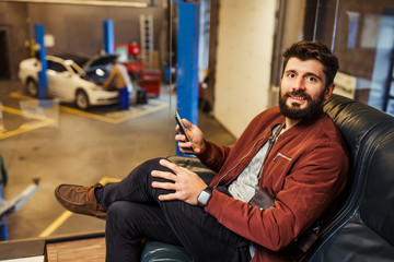 overhead view of smiling man with smartphone in the hand looking at the camera in a waiting room of the auto service center