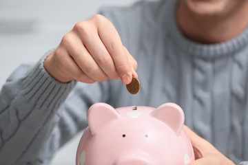 Obraz na płótnie Canvas Man putting coin into piggy bank on light background, closeup