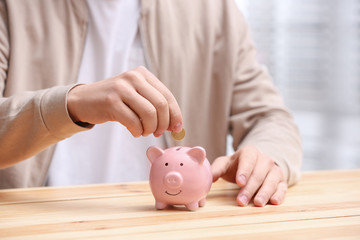 Obraz na płótnie Canvas Man putting coin into piggy bank at wooden table, closeup