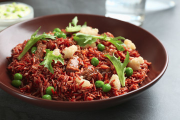 Tasty brown rice with meat and vegetables on dark grey table, closeup