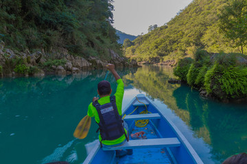 TAMUL, SAN LUIS POTOSI MEXICO - January 6, 2020: Rear view of man in raincoat and vest rowing in canoe. Active, adventure, outdoors, in tamul river