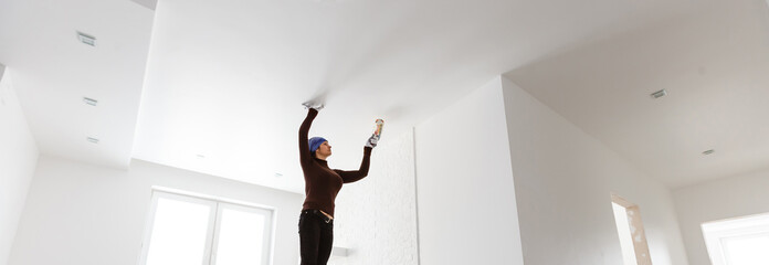 Woman paints ceiling with brush at home