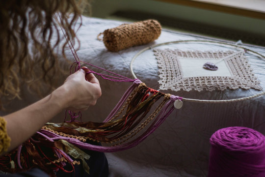 Back view of crop woman creating handmade dreamcatcher with long threads spending time in house