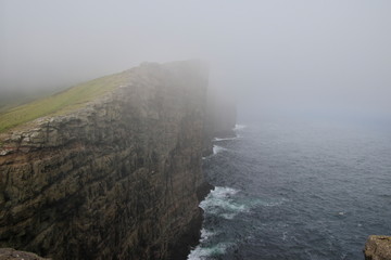 Fototapeta na wymiar Scenic vertical image to cliffs and North Atlantic Ocean covered by fog near the lake Sørvágsvatn or Leitisvatn Lake on Island Vágar of the Faroe Islands