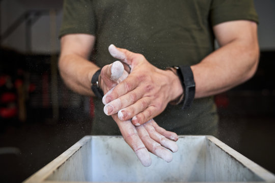Strong man prepares to exercise in the gym with magnesium in his hands. Young athlete practicing multidisciplinary training
