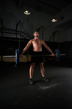 Strong man with barbell with weights in his hands doing strength exercises in the gym with magnesium in his hands. Young athlete practicing multidisciplinary training
