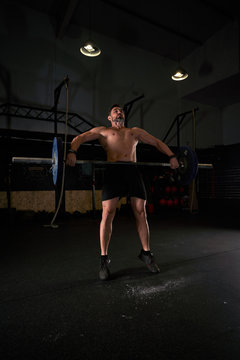 Strong man with barbell with weights in his hands doing strength exercises in the gym with magnesium in his hands. Young athlete practicing multidisciplinary training