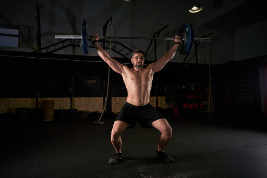 Strong man with barbell with weights in his hands doing strength exercises in the gym with magnesium in his hands. Young athlete practicing multidisciplinary training