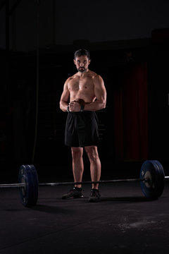 Strong man with barbell with weights in his hands doing strength exercises in the gym with magnesium in his hands. Young athlete practicing multidisciplinary training