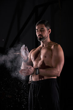 Strong man preparing strength exercises in the gym with magnesium in his hands. Young athlete practicing multidisciplinary training