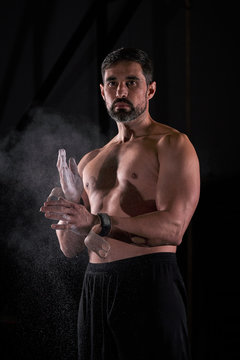 Strong man preparing strength exercises in the gym with magnesium in his hands. Young athlete practicing multidisciplinary training