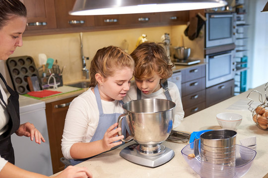 Stock photo of children in aprons looking at a container in the kitchen and preparing cupcake